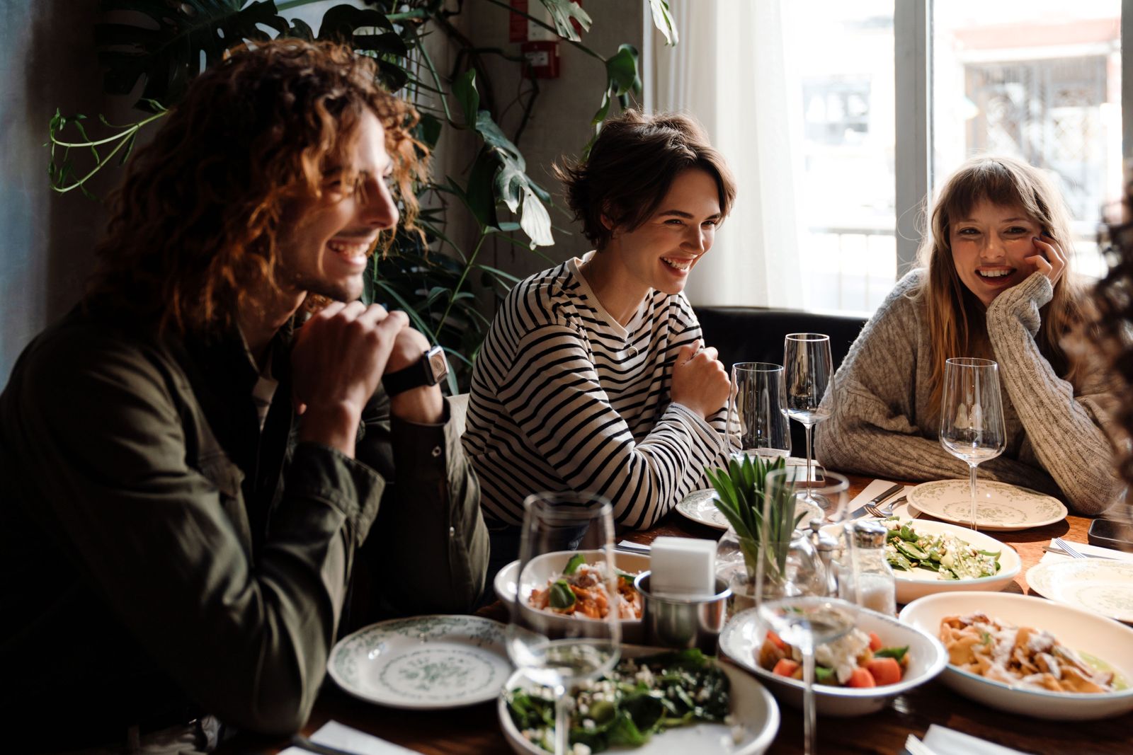 Three people sat around a table of small plates laughing